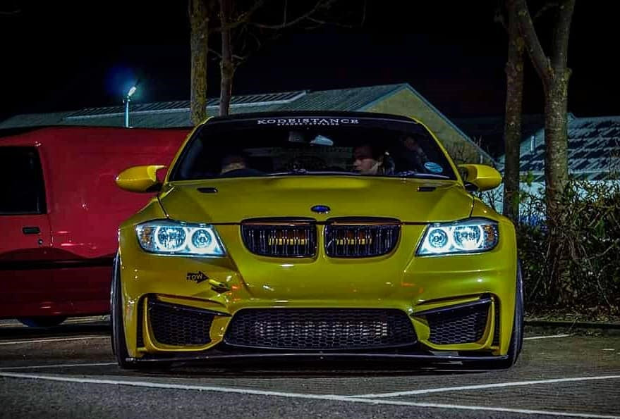 Front view of gold BMW 3 Series E90 with M4 Look front bumper, custom grille, and LED headlights at night.