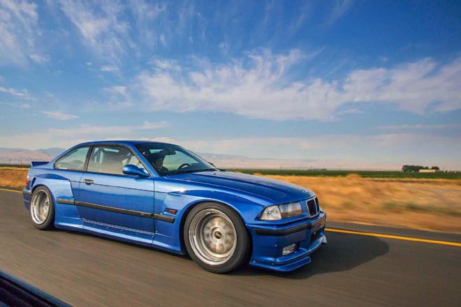 BMW E36 Coupe on the road with Rocket Bunny style body kit featuring wide arches and aerodynamic enhancements.