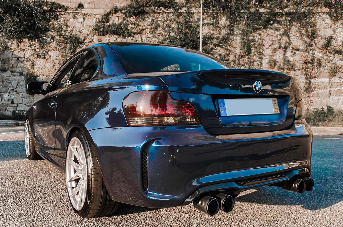 Rear bumper BMW 1 Series E82 E88 M2 Look installed on a dark blue coupe, featuring a quad exhaust setup and sporty diffuser design.