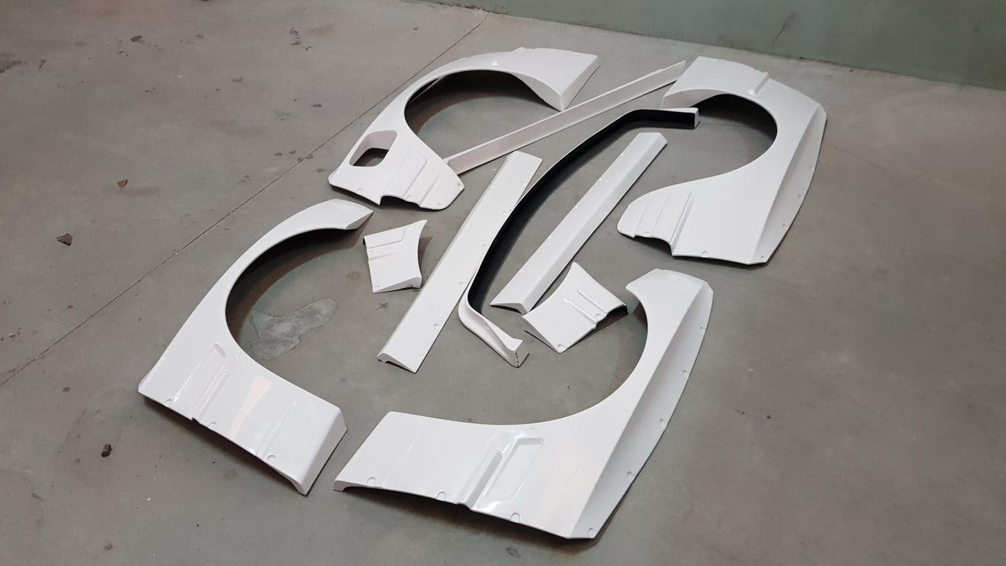Rocket Bunny wide body kit parts for BMW E30 Coupe laid on the floor, showing fenders, side skirts and bumper extensions in white.
