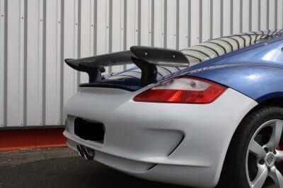 TRUNK SPOILER PORSCHE CAYMAN fitted on a blue and silver Porsche Cayman, shown from the rear three-quarter view