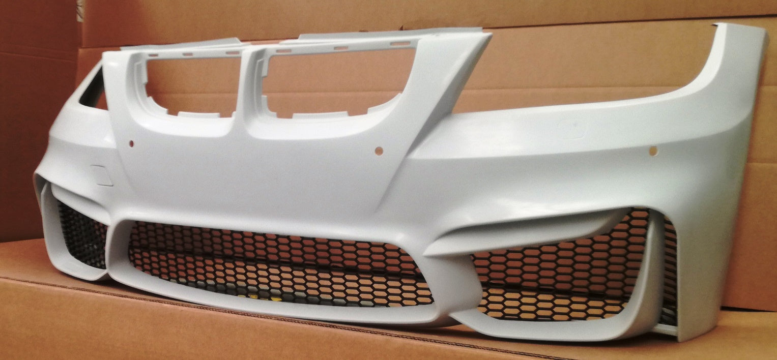 Unpainted BMW 3 Series E90/E91 M4 Look front bumper part with honeycomb grille design displayed on cardboard.