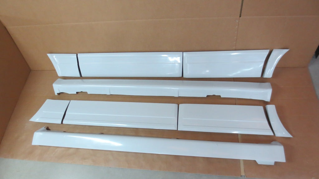 Set of white BMW E30 M-Technic side skirts and door panels for 4-door models displayed on the floor.