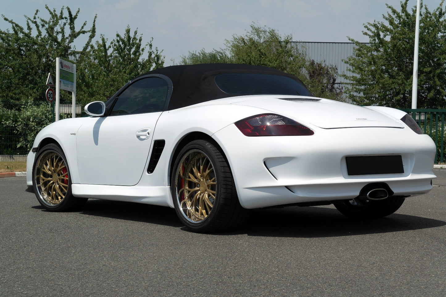 White Porsche Boxster 987 featuring a GT3 Look rear bumper, gold multi-spoke wheels, central exhaust outlet, and black convertible soft top.